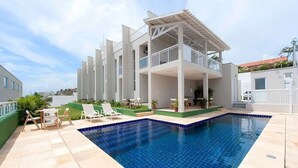 A modern building with a pool, outdoor seating, and a covered patio area. - Beach Townhouses I - Triplex by Carpediem (Aquiraz)
