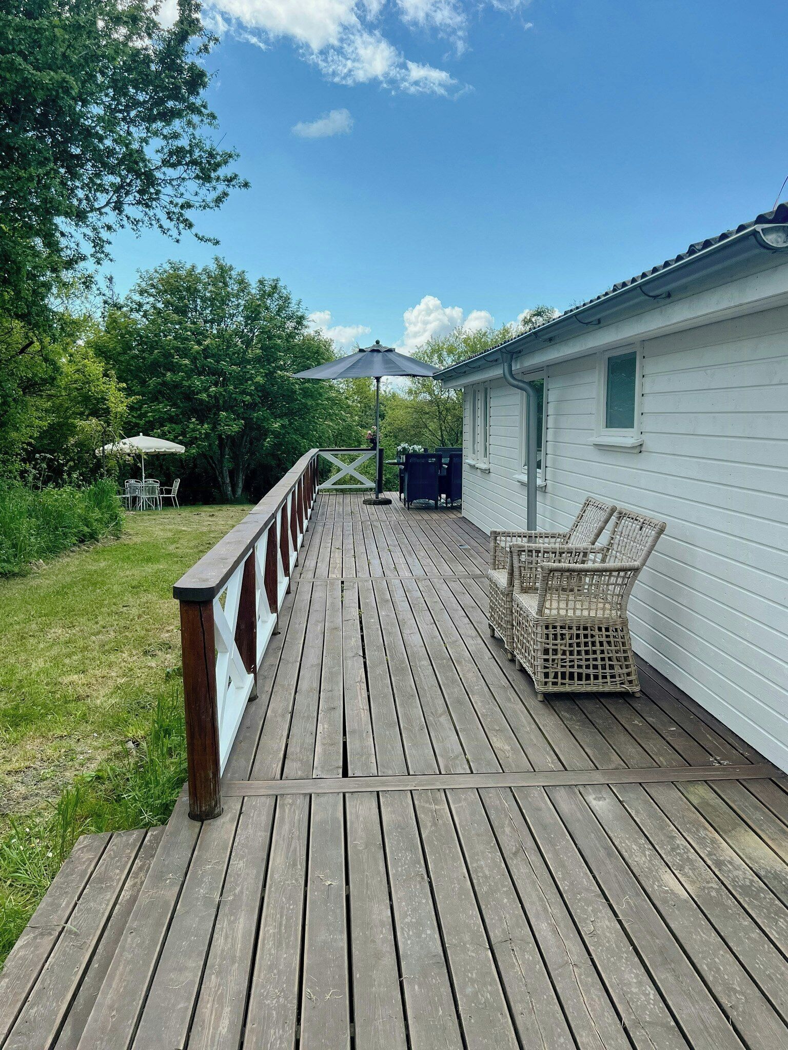 A wooden deck leading to a white building with a window, a covered outdoor seating area, and a railing.