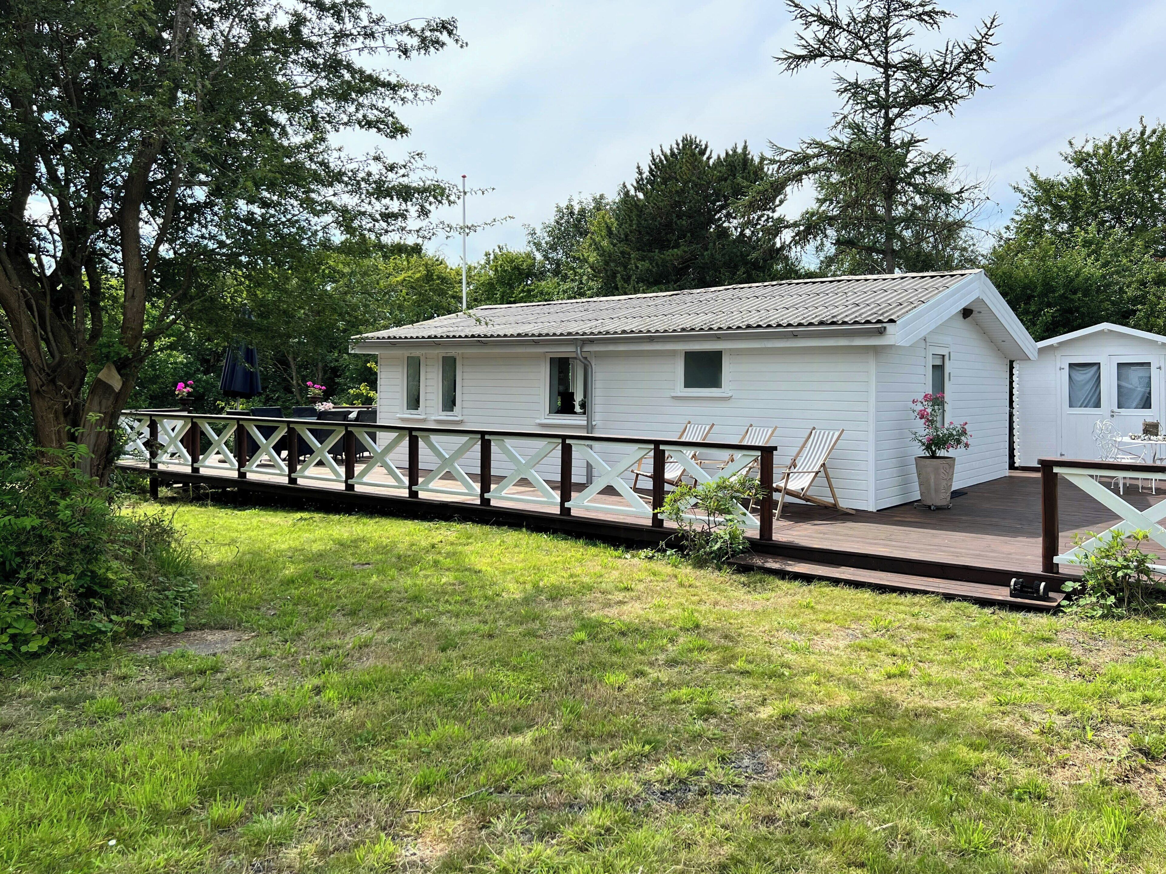 A white cabin with a deck, surrounded by greenery.