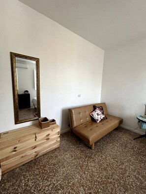 A room with a brown sofa, a wooden dresser, a mirror, and a small round table. - Small attic with romantic terrace in the heart of Torpignattara. (Roma)