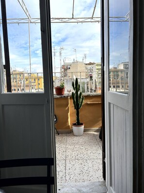 A balcony with a potted cactus and a potted plant, a tiled floor, and a view of buildings in the background. - Small attic with romantic terrace in the heart of Torpignattara. (Roma)
