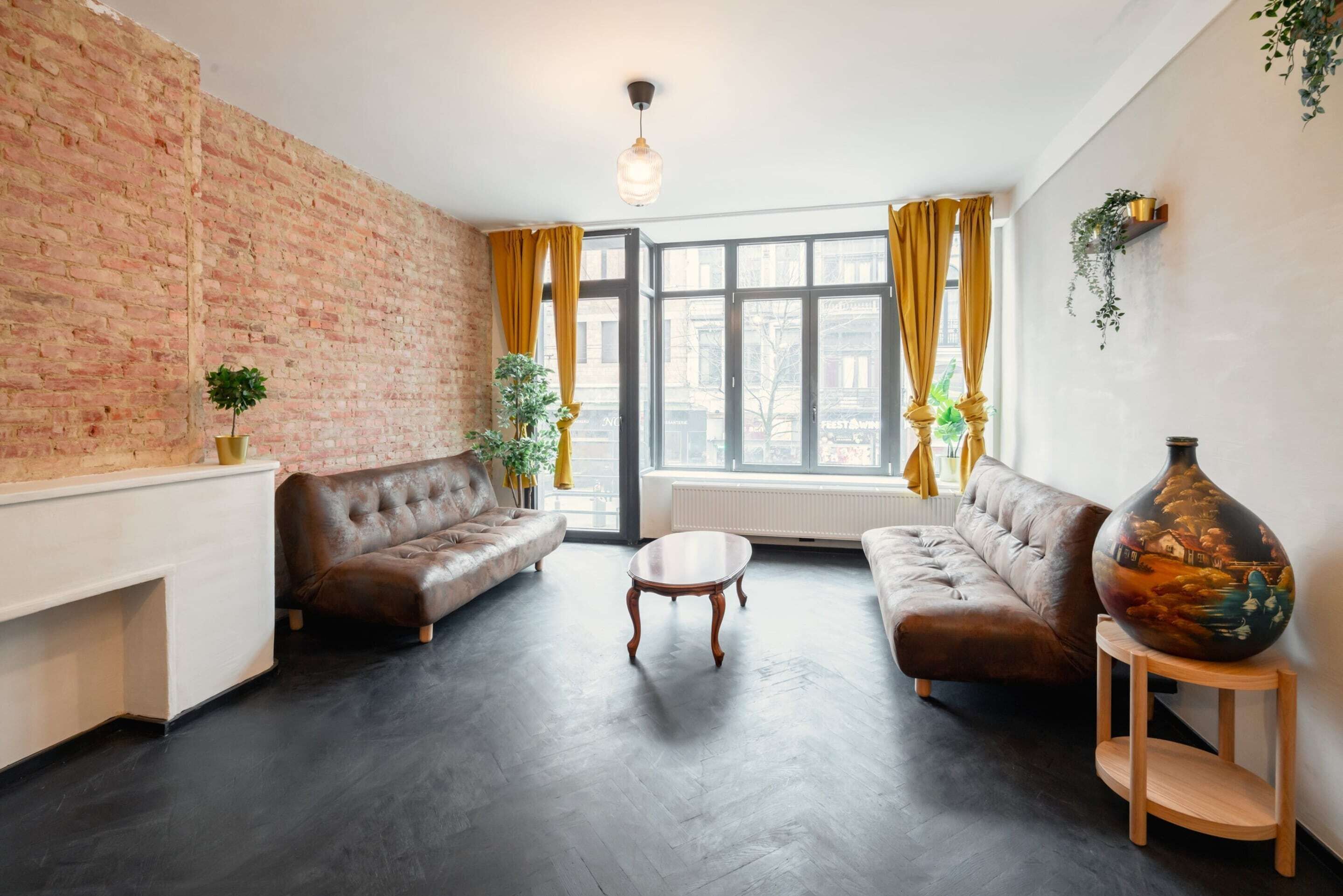 Ein Wohnzimmer mit Backsteinwand, zwei Sofas, einem Couchtisch und einer großen Vase.