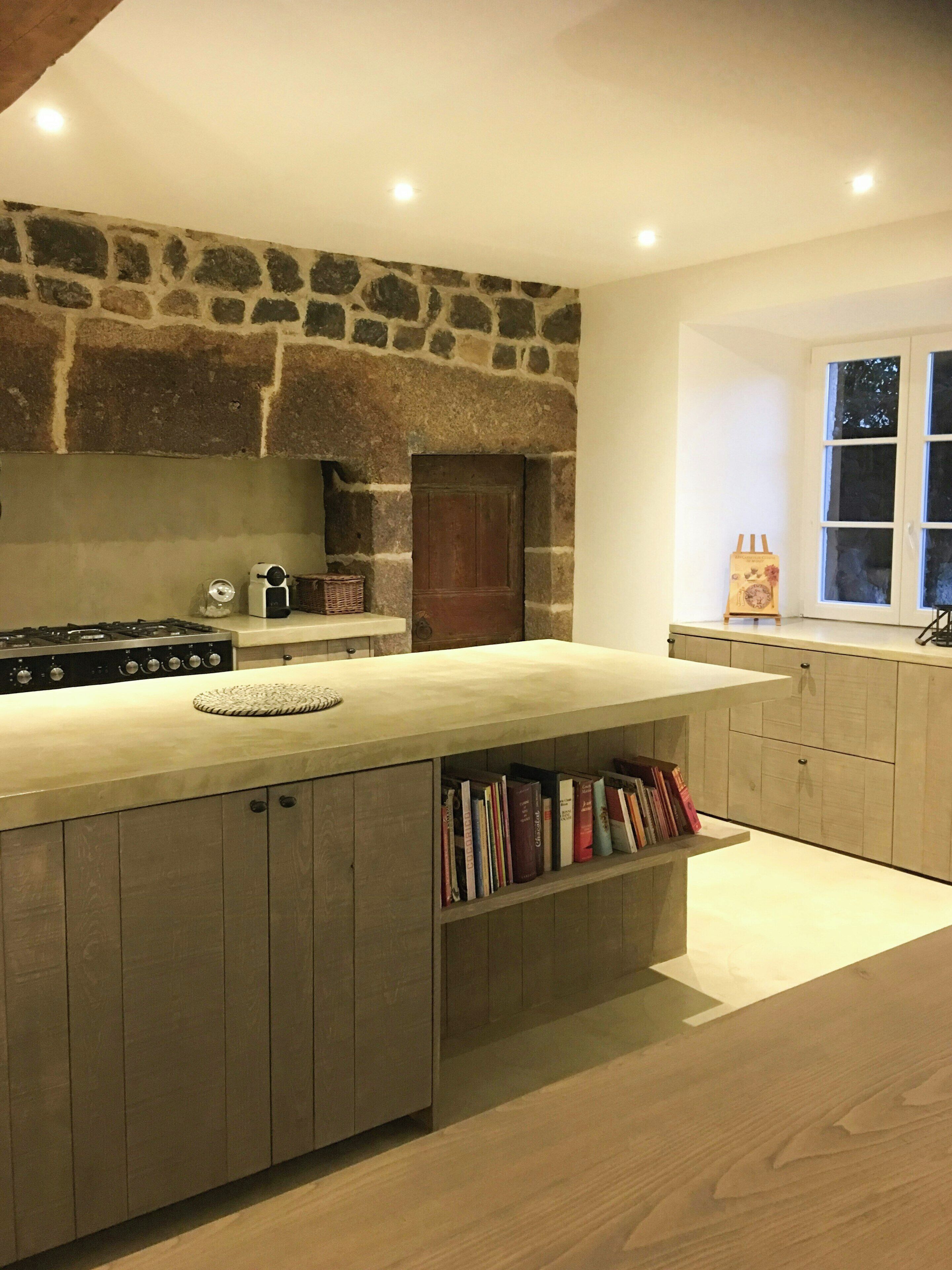 Una cocina con pared de piedra, puerta de madera, estantería empotrada y ventana con cortinas.