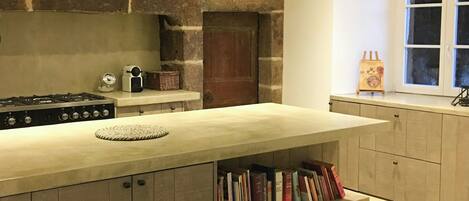 Una cocina con pared de piedra, puerta de madera, estantería empotrada y ventana con cortinas.