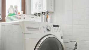 A front-loading washing machine with a control panel, a wall-mounted heater, and a window with a view.