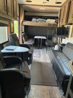 Interior compacto de uma motorhome, com sofá, duas cadeiras, uma mesinha e beliche.