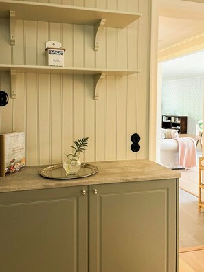 A kitchen with wooden cabinets, a countertop, and a shelf with a white container. - Historical grandma’s house at Rangsta Farm (Sorunda)