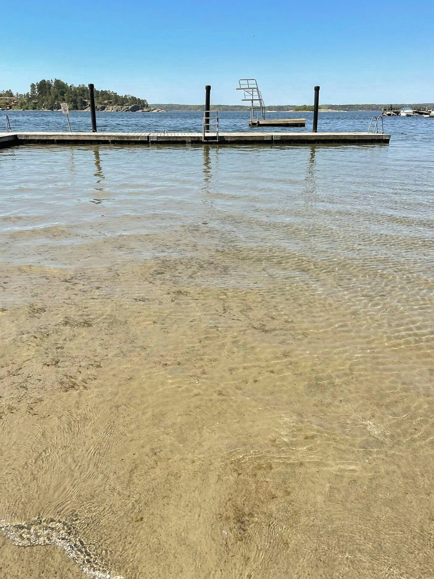 A clear waterfront view with a dock, a lifeguard stand, and a distant shoreline.