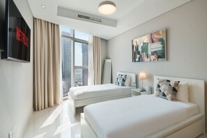 Ein Hotelzimmer mit zwei Betten, einem Fernseher, einem Gemälde und einem Fenster mit Blick auf die Stadt.