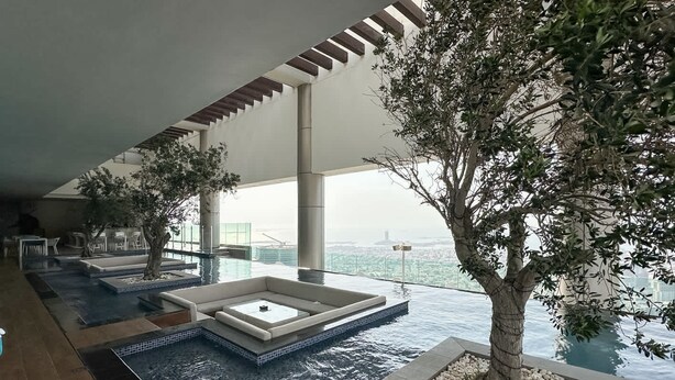 A modern indoor pool area with multiple water features, seating areas, and a large tree. - Chic 2BR in Paramount Midtown Infinity Pool Access (Dubai)