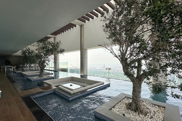 Ein moderner Poolbereich im Innenbereich mit verschiedenen Wasserspielen, Sitzgelegenheiten und einem großen Baum.