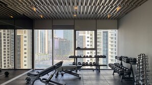 A gym with exercise equipment, large windows, and a view of high-rise buildings. - Chic 2BR in Paramount Midtown Infinity Pool Access (Dubai)