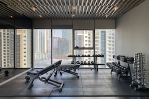Ein Fitnessstudio mit Trainingsgeräten, großen Fenstern und Blick auf hohe Gebäude.