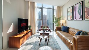 A modern living room with a large TV, a sofa, a coffee table, and a view of tall buildings. - Chic 2BR in Paramount Midtown Infinity Pool Access (Dubai)