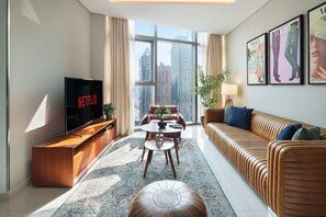 Ein modernes Wohnzimmer mit großem Fernseher, einer Couch, einem Couchtisch und Blick auf hohe Gebäude.
