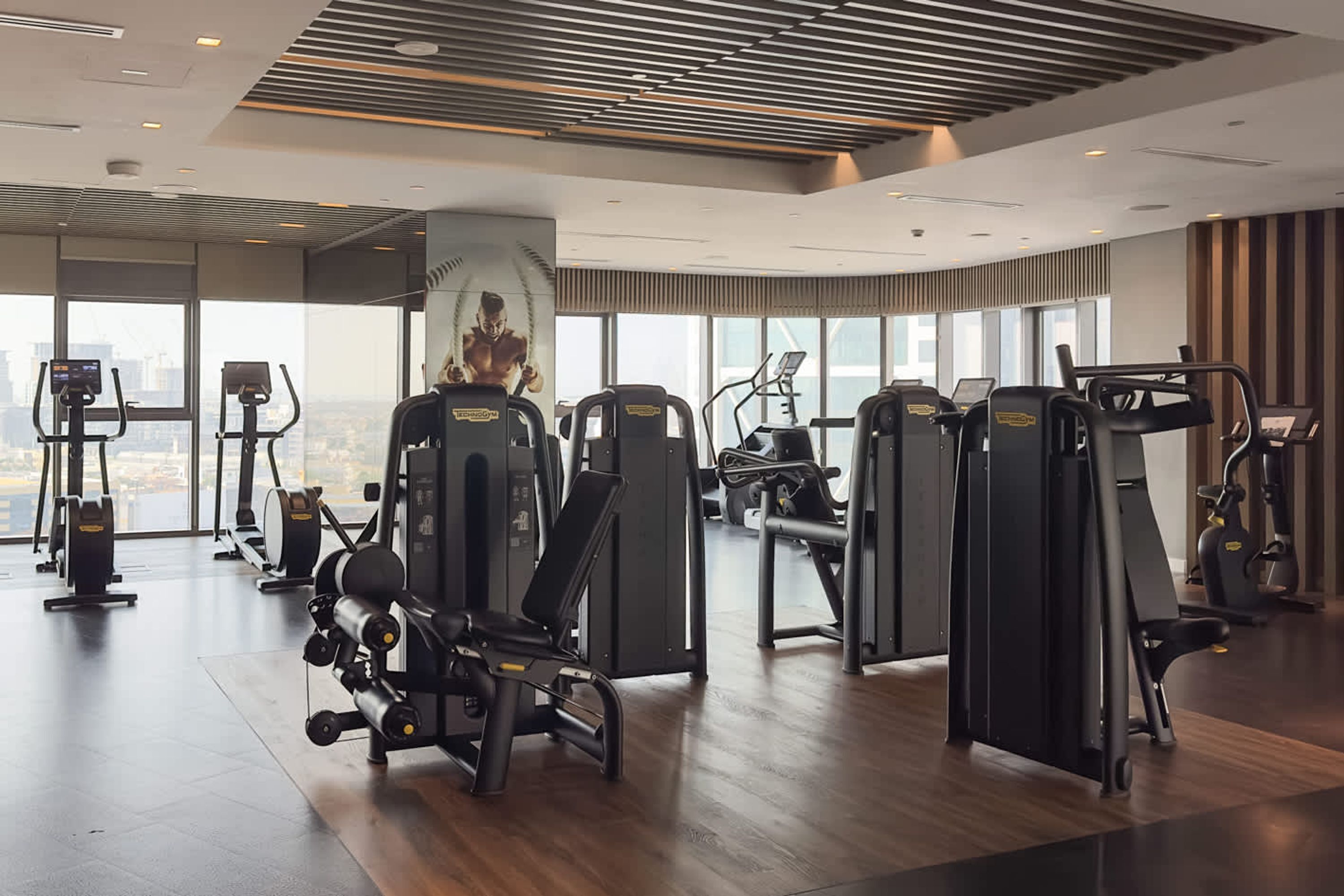 A modern gym with various exercise machines, large windows, and a city view.