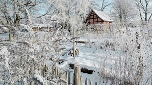 Et sneklædt landskab med et traditionelt træhus, en træhegn og snebelastede træer.