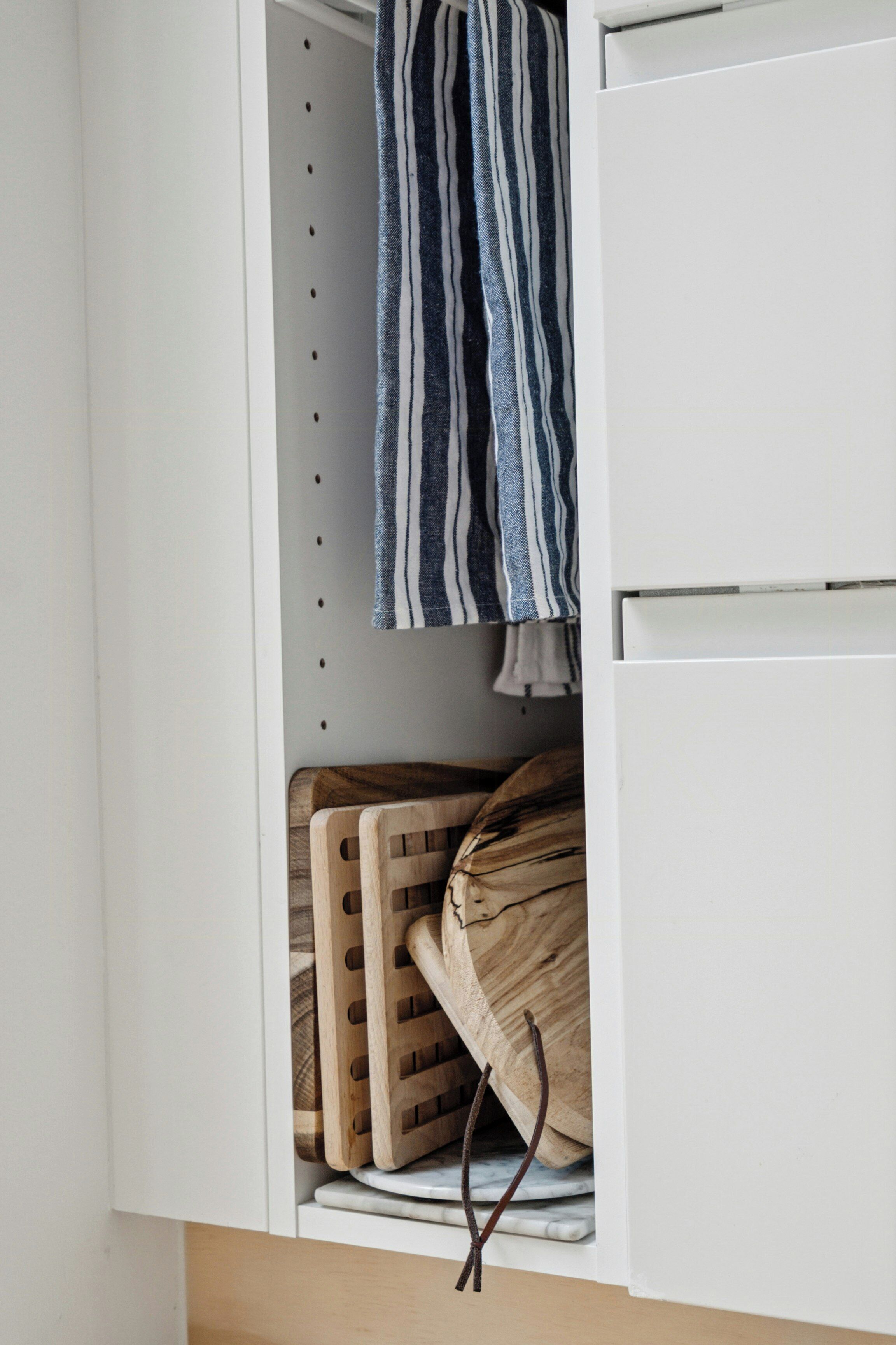 A kitchen cabinet with wooden cutting boards and a striped towel.