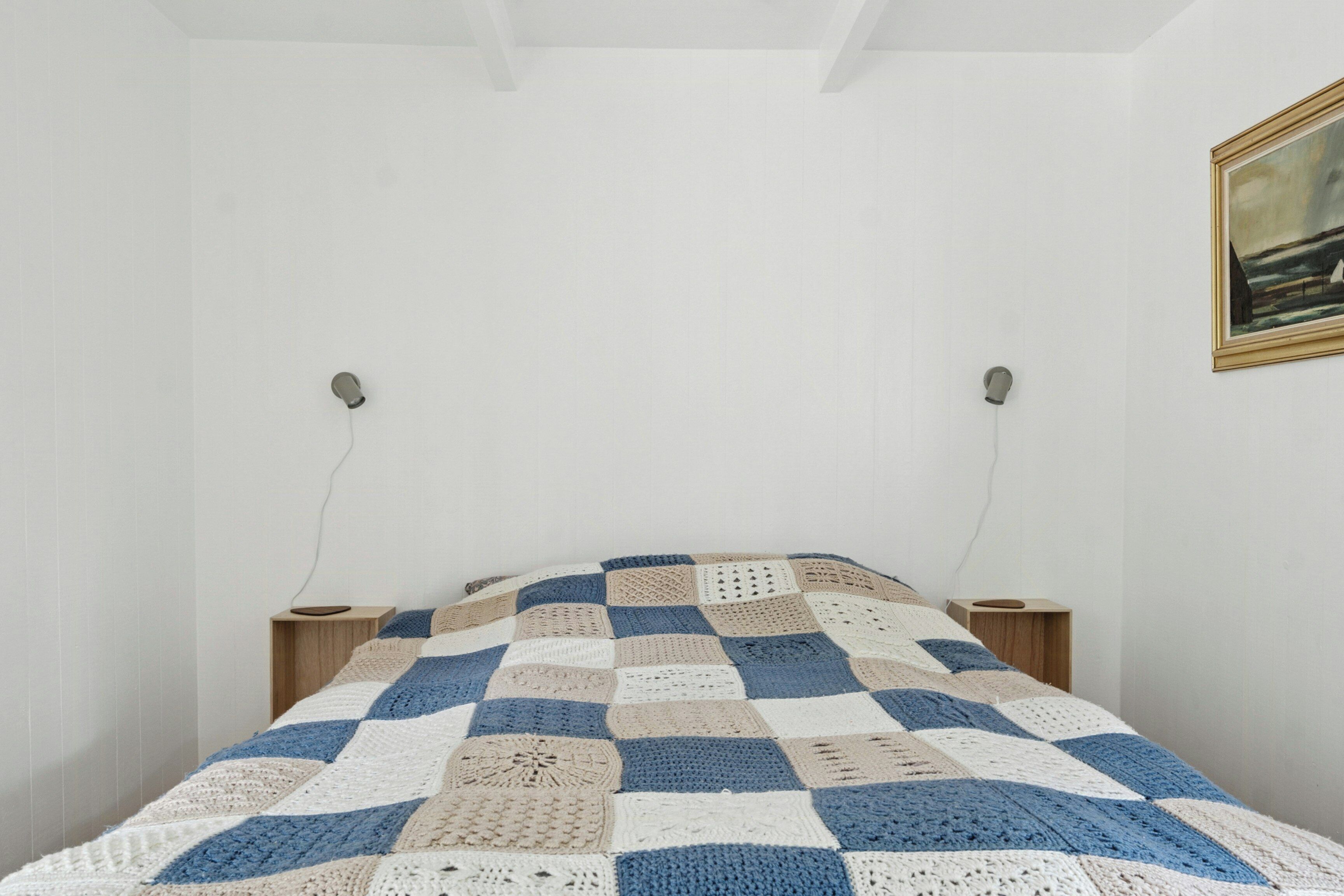 A bedroom with a checkered blanket, two bedside tables, and a framed picture on the wall.