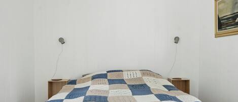 A bedroom with a checkered blanket, two bedside tables, and a framed picture on the wall.