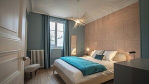 A bedroom with a bed, a bedside table, a lamp, a window with curtains, and a radiator. - Modern villa with spa in the heart of Alsace (Selestat)