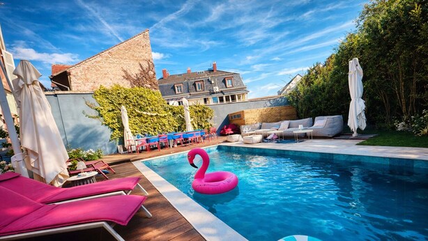 A swimming pool with lounge chairs, a flamingo float, and a view of a building in the background. - Modern villa with spa in the heart of Alsace (Selestat)
