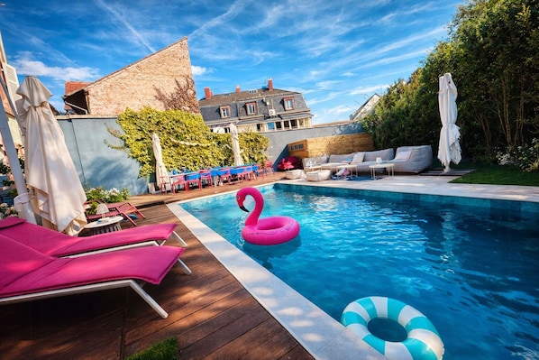 Ein Schwimmbecken mit Liegestühlen, einem Flamingo-Badeschwimmer und Blick auf ein Gebäude im Hintergrund.