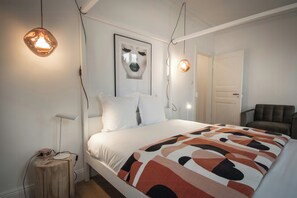 A bedroom with a bed, a wooden side table, a chair, and a framed artwork on the wall.