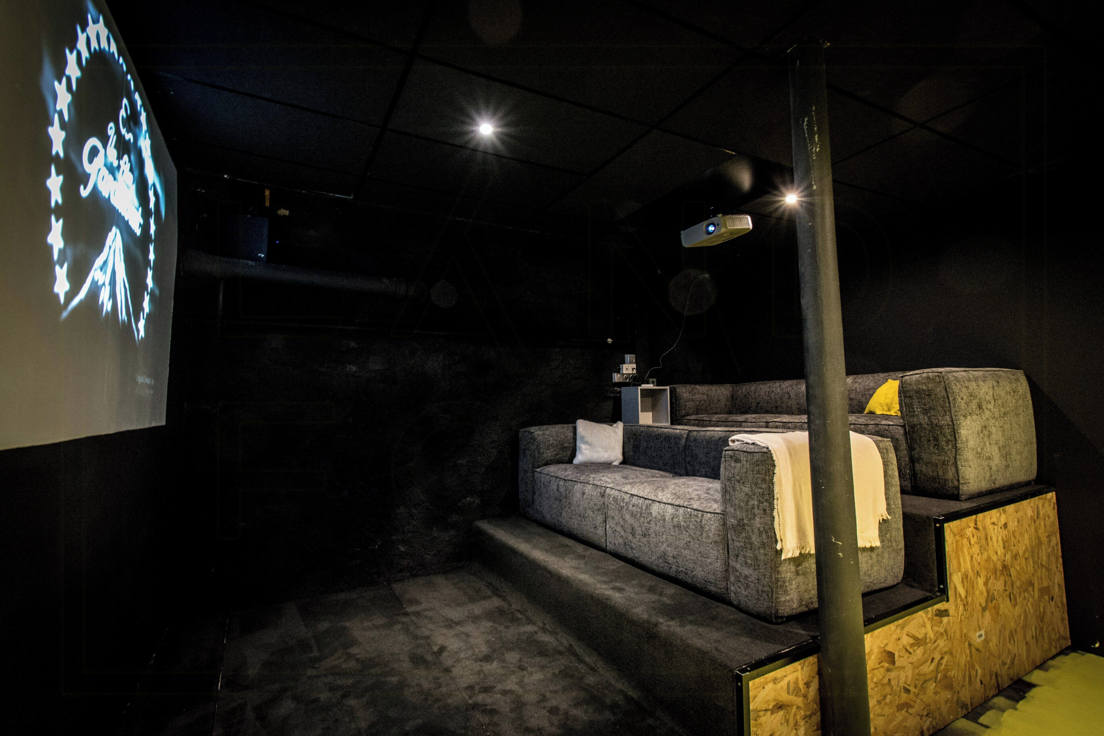 A dark room with a projection screen displaying a circular design, a couch, and a wooden structure.