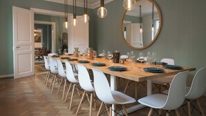 A dining area with a long wooden table, white chairs, and hanging pendant lights. - Modern villa with spa in the heart of Alsace (Selestat)