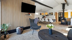 Una sala de estar moderna con un televisor de pantalla plana, una mesa redonda de madera y un área de estar acogedora.
