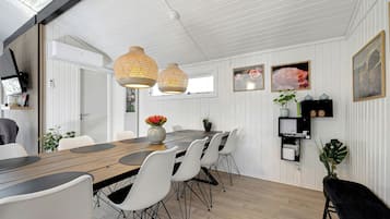 Un espace repas avec une table en bois, des chaises blanches et des luminaires suspendus.