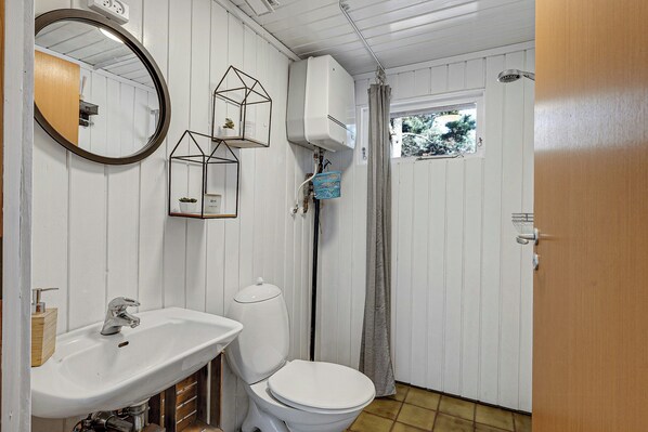 A bathroom with a white sink, toilet, and mirror. There is a window with a view of trees, and a shower with a curtain.