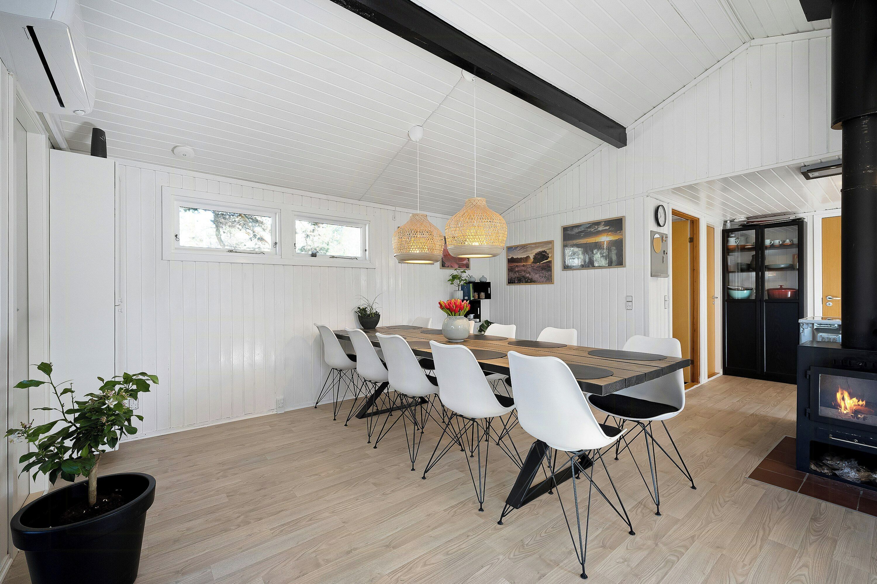 Un coin repas avec une table en bois, des chaises blanches, des luminaires suspendus et un poêle à bois noir.