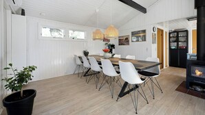 Un comedor con mesa de madera, sillas blancas, lámparas colgantes y un estufa de leña negra.