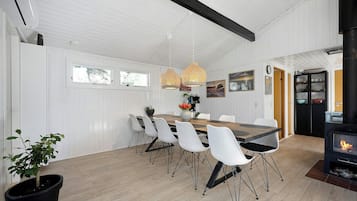 Un coin repas avec une table en bois, des chaises blanches, des luminaires suspendus et un poêle à bois noir.