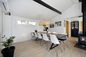 A dining area with a wooden table, white chairs, pendant lights, and a black wood-burning stove. - Idyllic gem on Als Odde with activities (Hadsund)