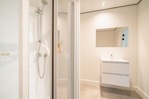 A modern bathroom with a glass shower enclosure, a white sink, and a mirror above it. - Cozy Antwerp City Apartment for 5 (Antwerp)