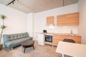 Ein kompakter Wohnbereich mit Sofa, kleinem Tisch und einer Küchenzeile, inklusive Kühlschrank, Backofen und Holzschränken.