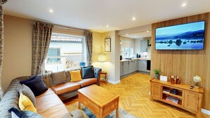 Een moderne woonkamer met een bank, salontafel en een aan de muur bevestigde televisie.