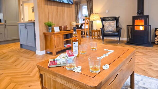Een gezellige woonkamer met een houten salontafel, boeken, glazen en een open haard.