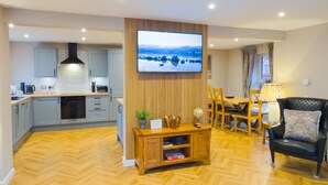 Een moderne woonkamer met een televisie, een houten tv-meubel en een eethoek met stoelen en een tafel.