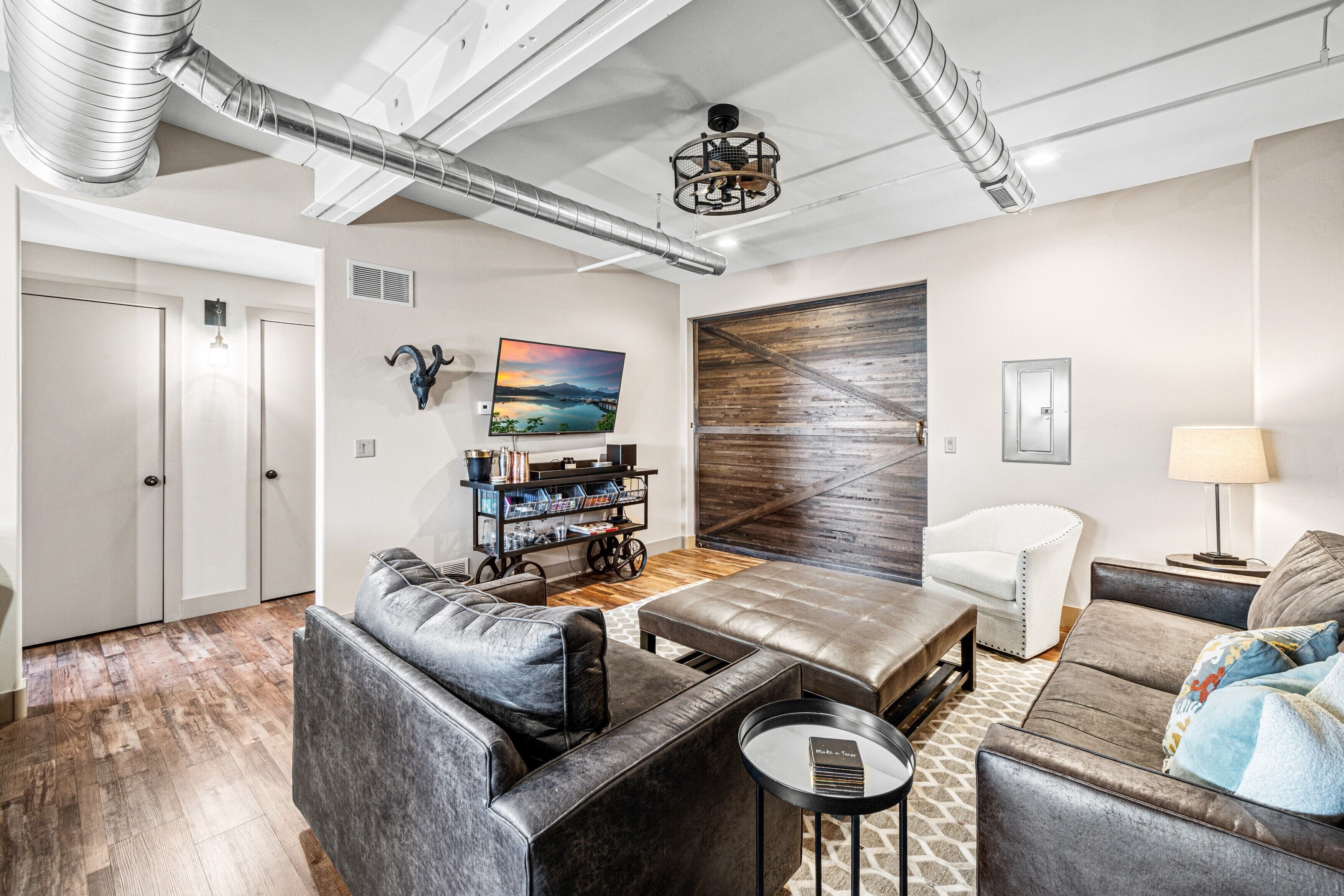 A modern living room with leather sofas, a wooden accent wall, a bookshelf, and a large window.