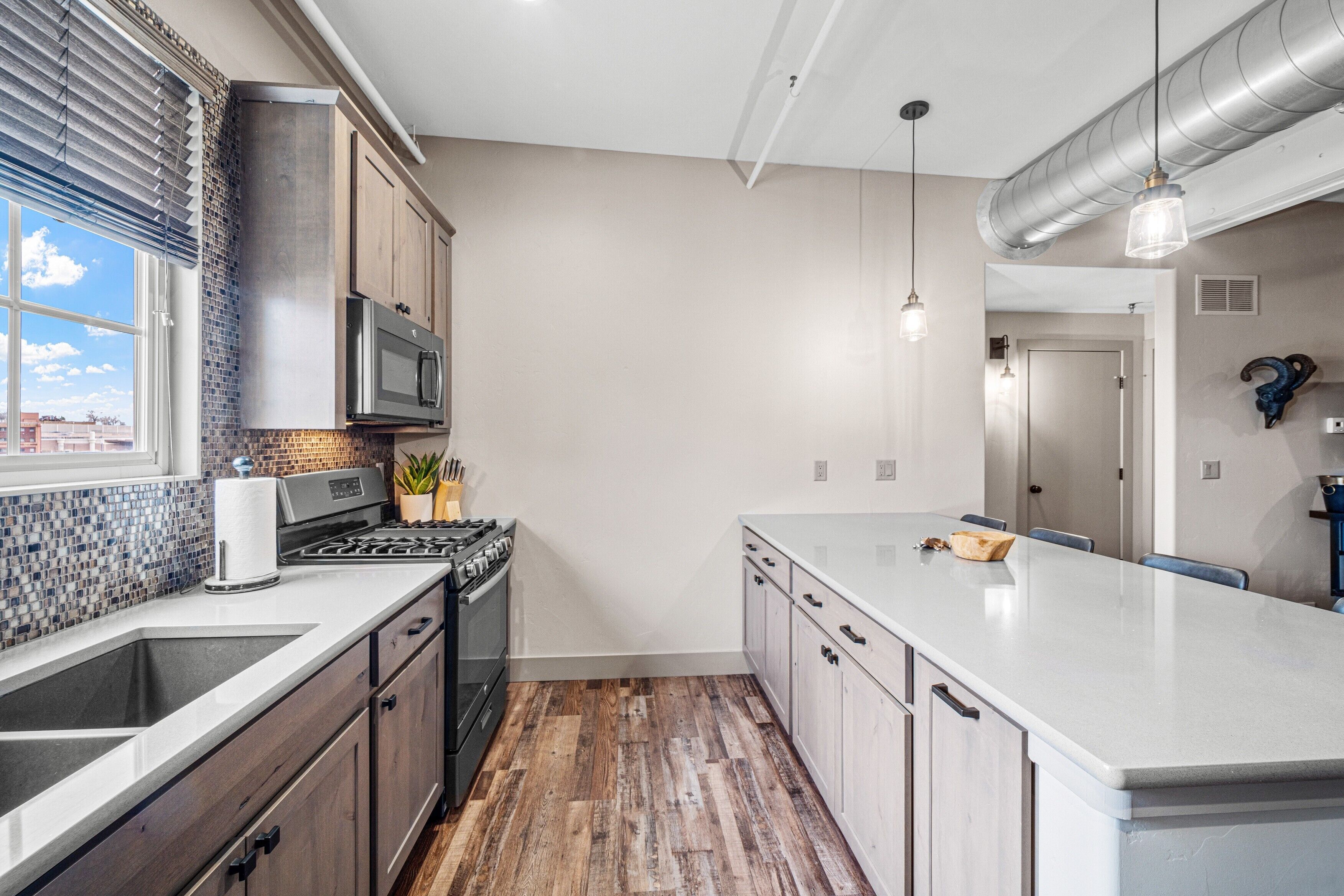 A modern kitchen with a large island, stainless steel appliances, and a wooden floor.