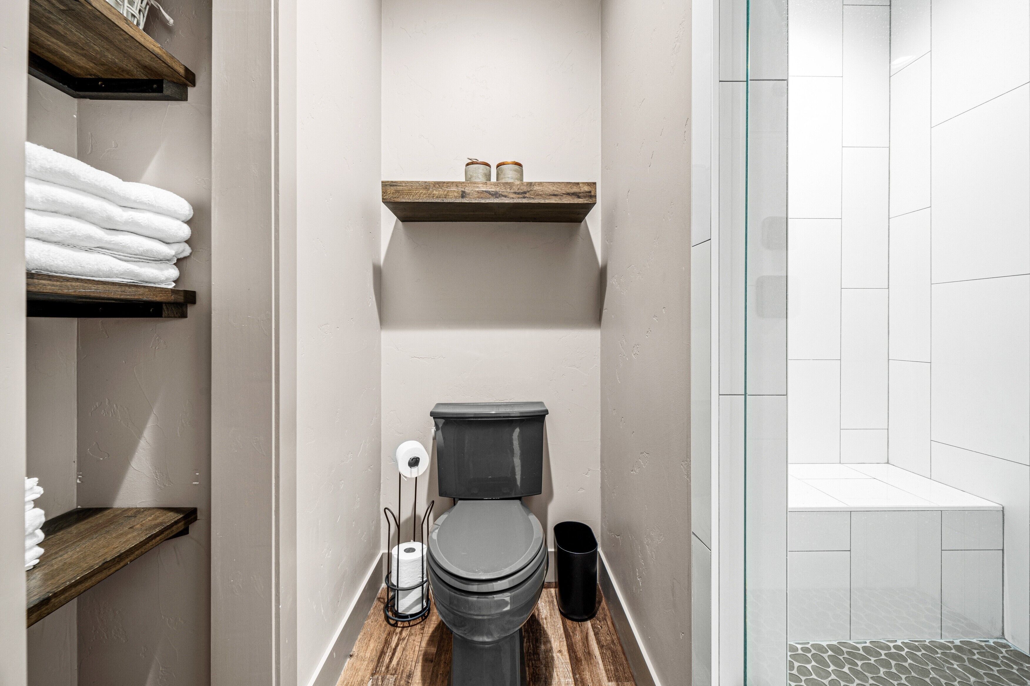 Un baño con inodoro, estantes con toallas y zona de ducha.