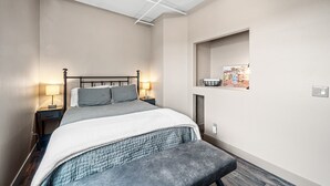 Ein Schlafzimmer mit einem Bett, Nachttischlampen, einer Bank, einem Wandregal und einer Deckenleuchte.