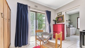 A room with a glass table, two chairs, a red cabinet, and a red rug. - The Cozy 1 Bedroom Apartment (Johannesburg)