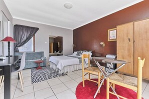 Ein Hotelzimmer mit Bett, Schreibtisch, Stuhl, Nachttisch, Kleiderschrank und einem Fenster mit Vorhängen.