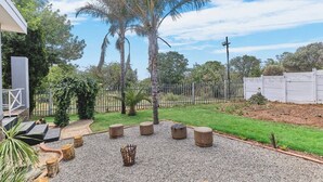 A patio with stone seating, a gravel area, and a fenced garden with palm trees. - The Cozy 1 Bedroom Apartment (Johannesburg)