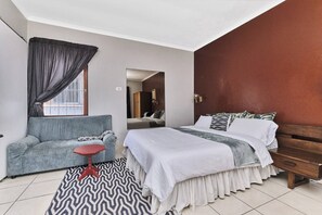 A bedroom with a bed, a sofa, a small table, and a patterned rug. - The Cozy 1 Bedroom Apartment (Johannesburg)